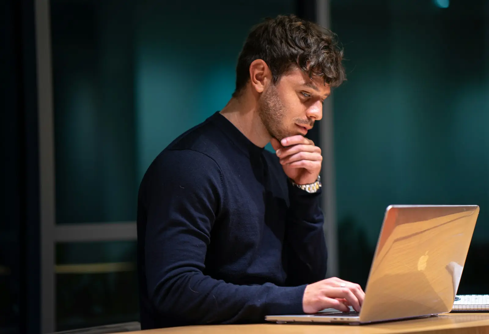 A man at his laptop, chin in hand, thinking.