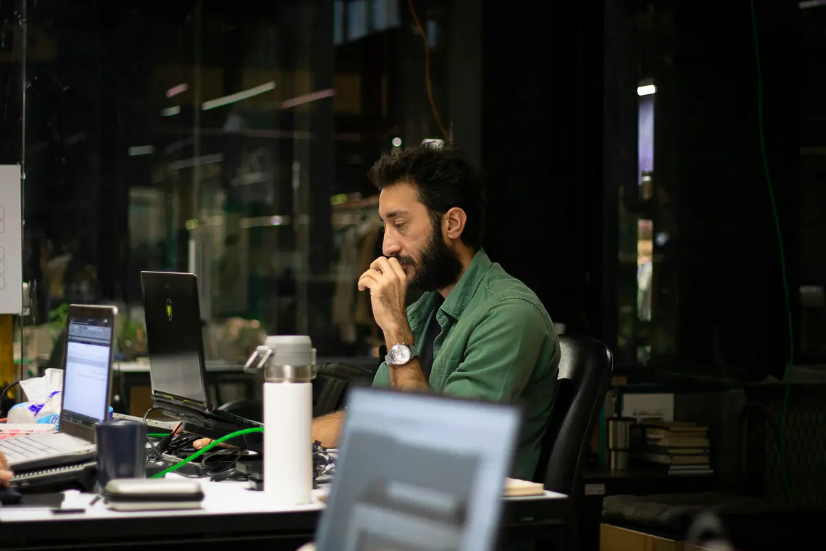 A man working late at his laptop in a dark office, head in his hand.